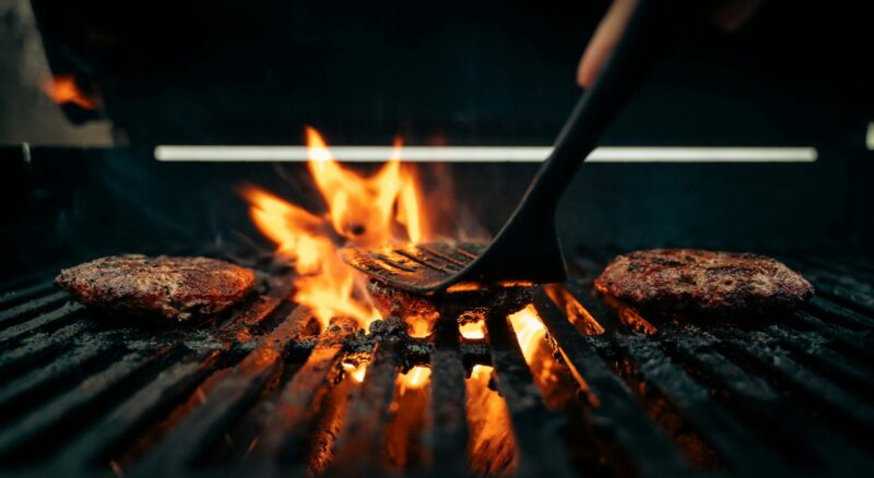 Vegan-Burger auf dem Grill mit Spatel, BBQ-Setting mit Holzkohle-Optik