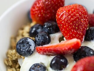 Verschiedene vegane Joghurts in Gläsern und Bechern mit Beeren, Haferflocken und Honig-Alternative