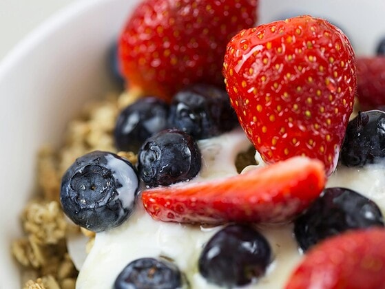 Verschiedene vegane Joghurts in Gläsern und Bechern mit Beeren, Haferflocken und Honig-Alternative