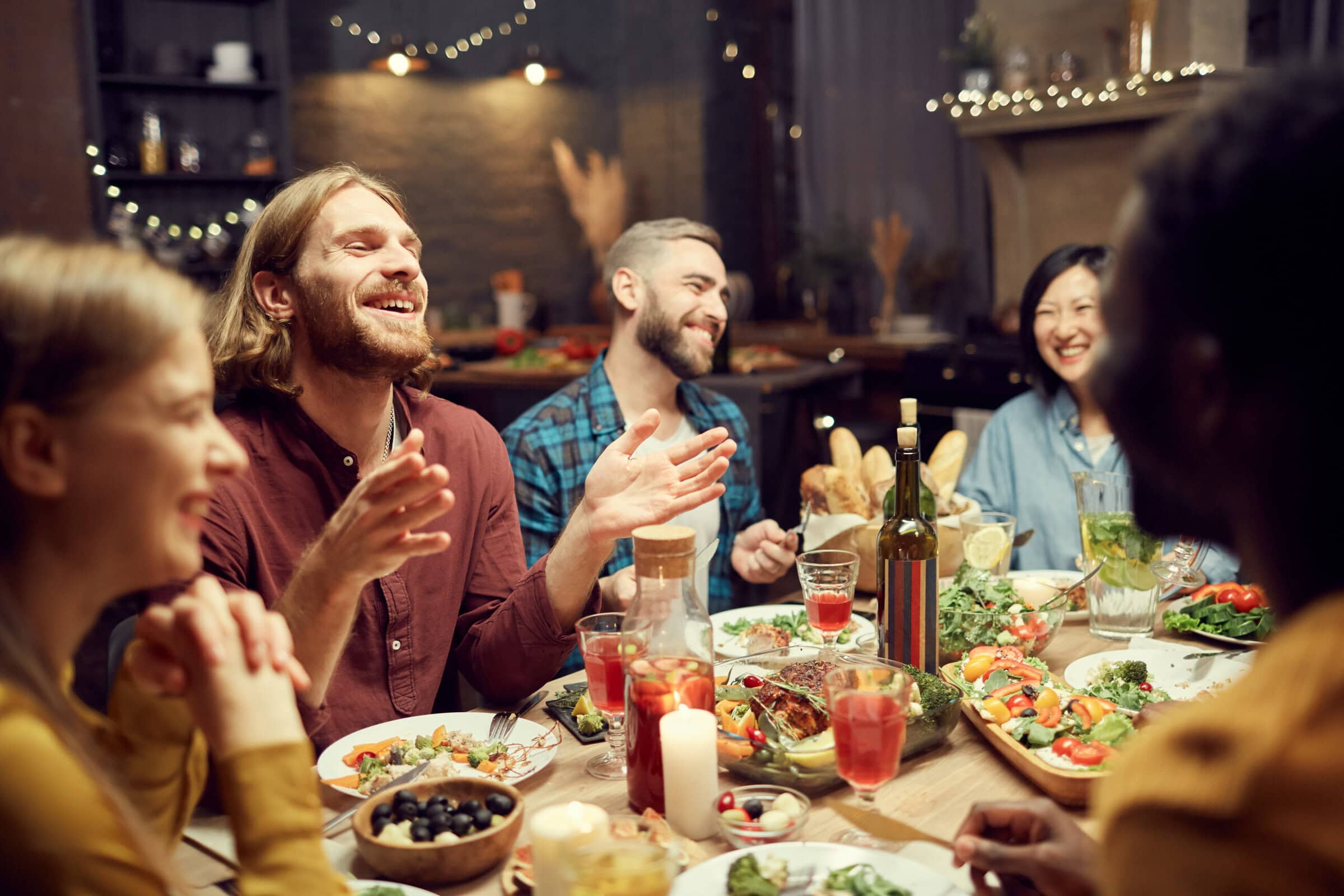 Freunde sitzen bei Kerzenschein an einem gedeckten Tisch mit Rotwein und vielen kleinen Gerichten