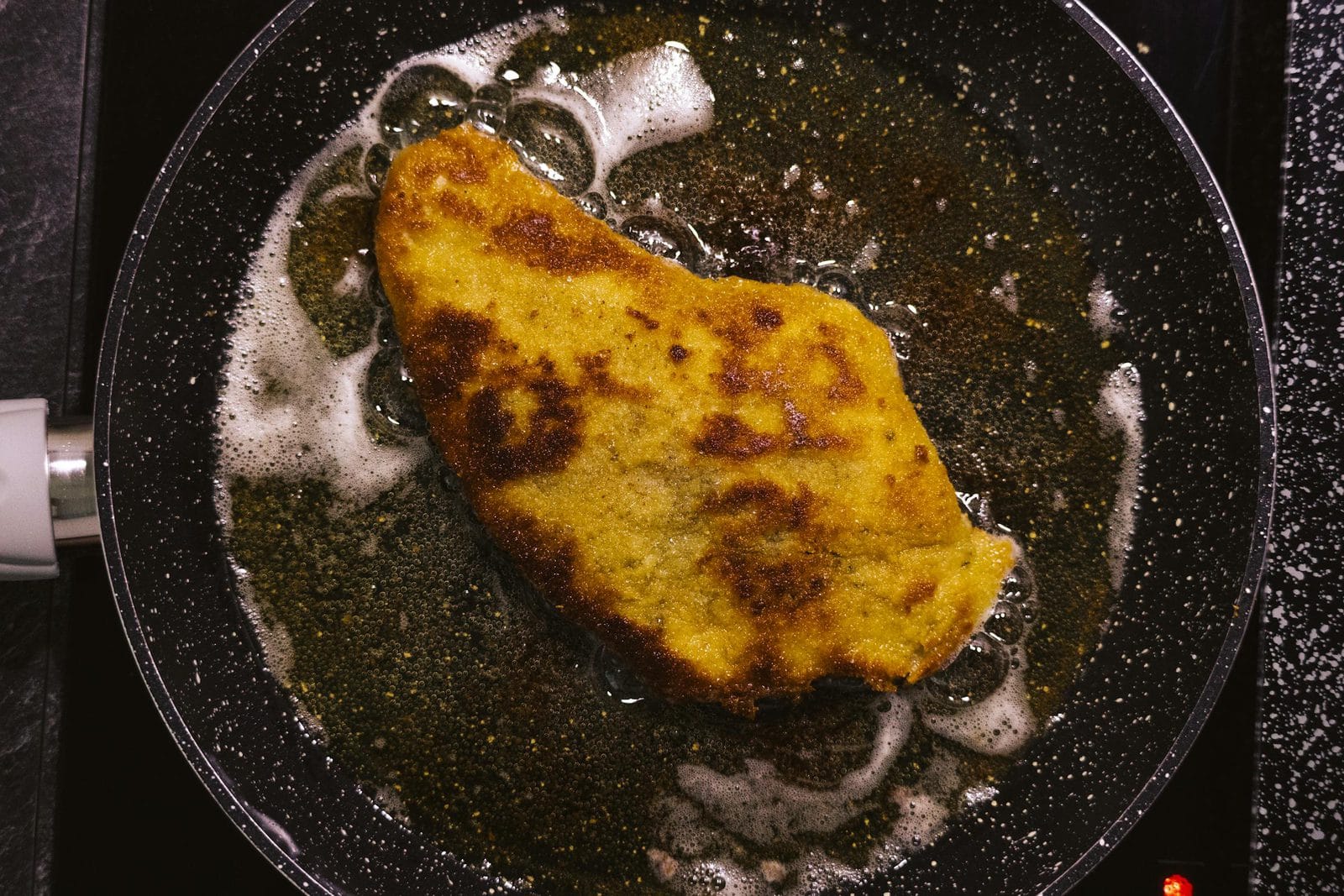 Goldgelbes Wiener Schnitzel auf weißem Teller mit Zitronenscheibe und Petersilie