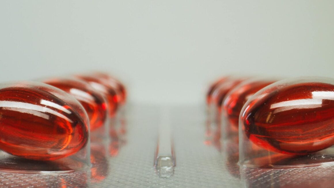Vitamin-B12-Supplement-Flasche mit roten Cyanocobalamin-Tabletten auf Holzbrett, daneben Bluttest-Röhrchen