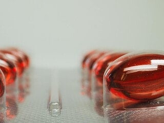 Vitamin-B12-Supplement-Flasche mit roten Cyanocobalamin-Tabletten auf Holzbrett, daneben Bluttest-Röhrchen
