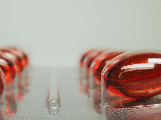 Vitamin-B12-Supplement-Flasche mit roten Cyanocobalamin-Tabletten auf Holzbrett, daneben Bluttest-Röhrchen
