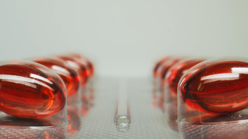 Vitamin-B12-Supplement-Flasche mit roten Cyanocobalamin-Tabletten auf Holzbrett, daneben Bluttest-Röhrchen