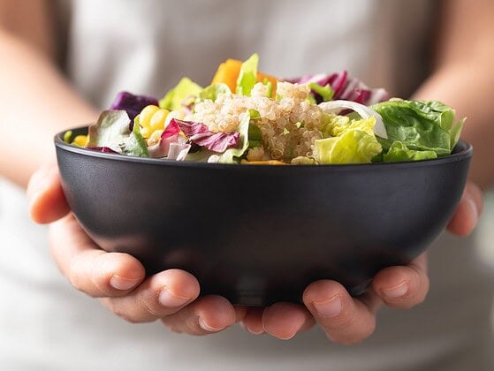 Bunte vegane Schale mit Hülsenfrüchten, Gemüse und Vollkorn auf hellem Holzbrett – evidenzbasierte vegane Ernährung