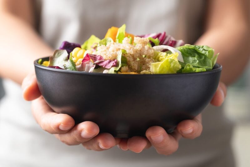 Bunte vegane Schale mit Hülsenfrüchten, Gemüse und Vollkorn auf hellem Holzbrett – evidenzbasierte vegane Ernährung