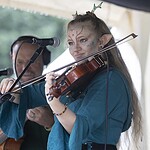 Vegan Fantasy Fair 2026 Geislautern: Die komplett pflanzliche Renfaire, auf die alle gewartet haben Bardinnen-Auftritt auf der Tavern Stage der Vegan Fantasy Fair: junge Violinistin im Elfen-Cosplay mit Geweih, blau-türkisem Mittelalter-Gewand und kunstvollem Face-Paint spielt Geige, im Hintergrund Begleitgitarrist.