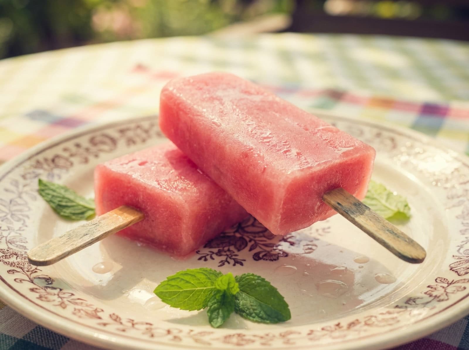 Pinkes Wassermelonen-Hundeeis am Holzstiel auf einem Vintage-Teller