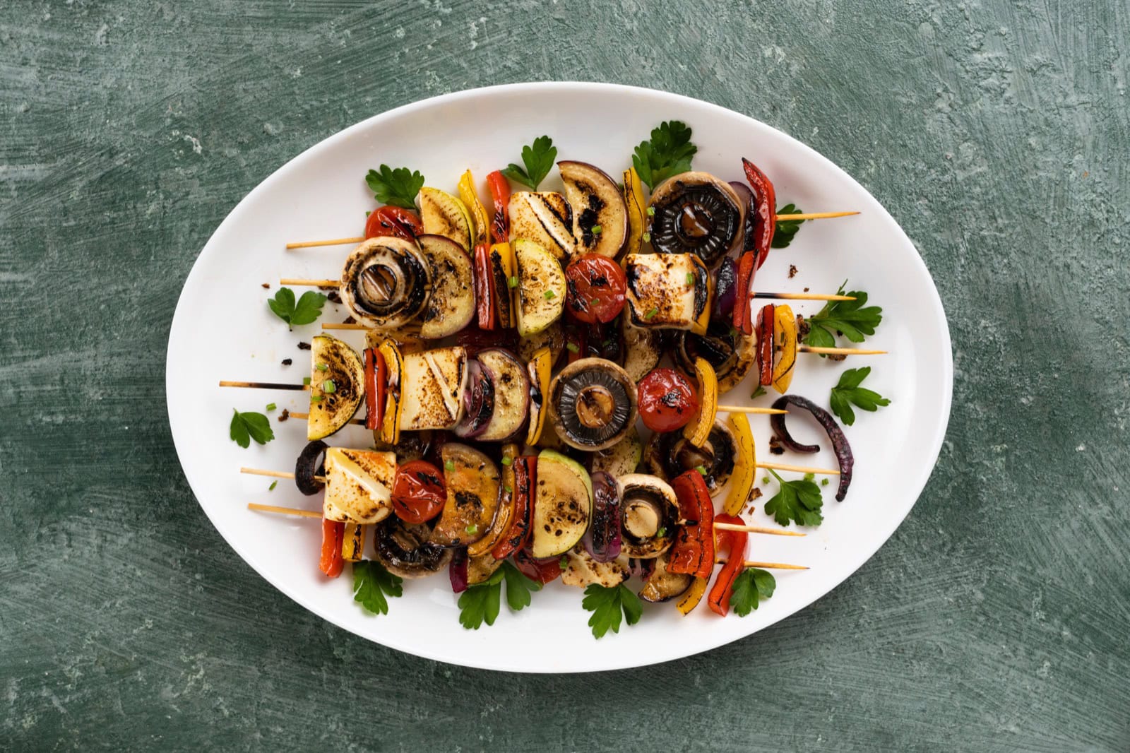 Vegane Grill-Spieße mit Tofu, Paprika, Zucchini und Champignons in einer weißen Schale, im Sommer-Outdoor-Setting