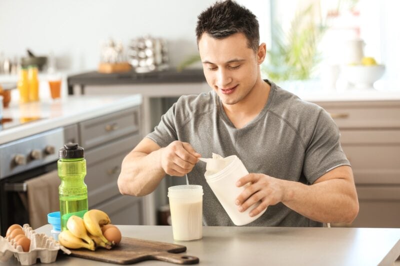 Sportlicher Mann macht zu Hause einen Protein-Shake nach dem Training