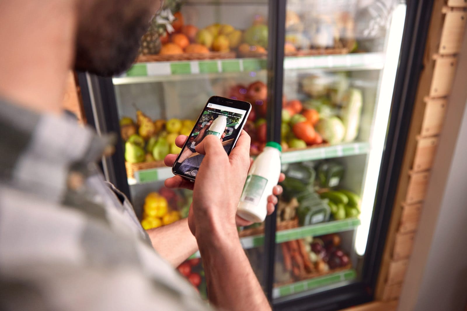 Person scannt mit dem Smartphone ein Produkt vor dem Kühlregal im Supermarkt