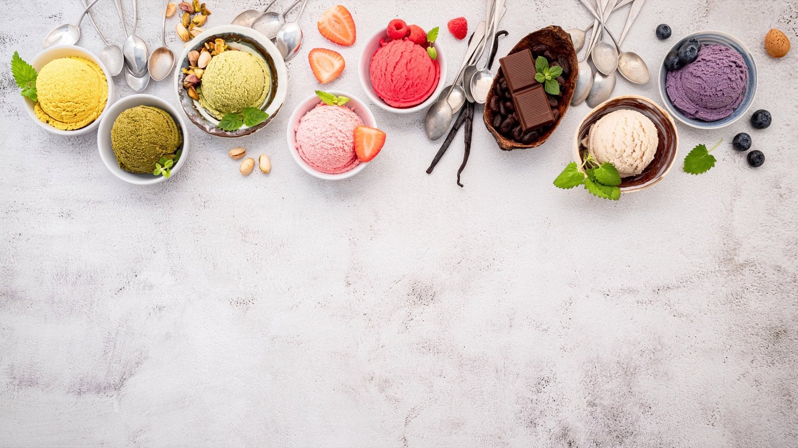 Vegane Eissorten in fünf Schüsseln: Blaubeere, Matcha, Kokos, Erdbeere und Schokolade auf hellem Stein-Untergrund