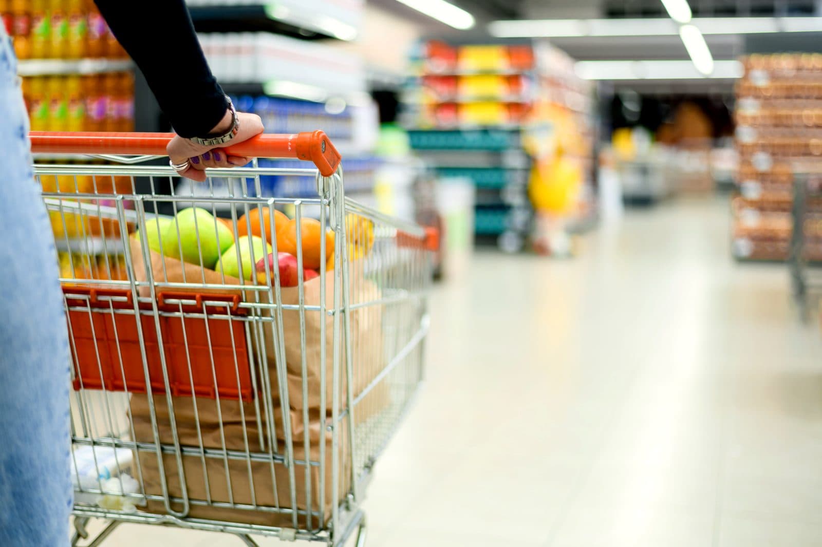 Voller Einkaufswagen mit Lebensmitteln wird durch einen Supermarktgang geschoben