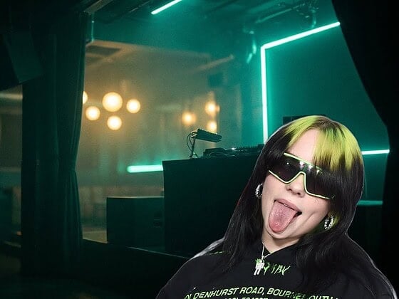 Billie Eilish with green sunglasses sticking out her tongue at an iHeartRadio event