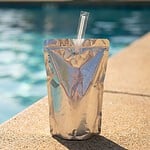 Ist Capri-Sonne vegan? Der ehrliche Check fürs Kult-Trinkpäckchen Silbernes Trinkpäckchen mit Strohhalm am Poolrand in der Sonne