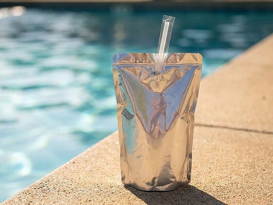 Silbernes Trinkpäckchen mit Strohhalm am Poolrand in der Sonne