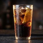 Ist Cola vegan? Der ehrliche Check für Coke, Fanta und Sprite Ist Cola vegan: Glas Cola mit Eiswürfeln und Zitronenscheibe vor dunklem Hintergrund