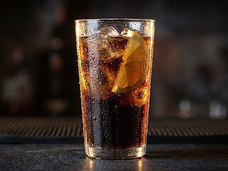 Ist Cola vegan: Glas Cola mit Eiswürfeln und Zitronenscheibe vor dunklem Hintergrund