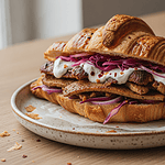 Döner Croissant vegan: So machst du dir den TikTok-Trend selbst Veganes Döner Croissant mit knusprigen Sojastreifen, Rotkohl, roten Zwiebeln und Knoblauchsauce auf einem Keramikteller