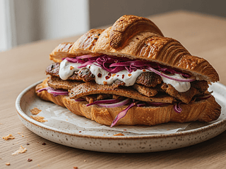 Veganes Döner Croissant mit knusprigen Sojastreifen, Rotkohl, roten Zwiebeln und Knoblauchsauce auf einem Keramikteller