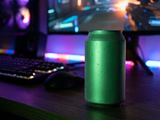 Grün leuchtende Energy-Drink-Dose mit Kondenswasser auf einem Schreibtisch vor einem Gaming-Setup