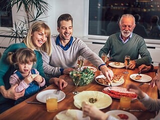 Mehrgenerationen-Familie beim gemeinsamen Essen am Esstisch mit grosser Salatschuessel