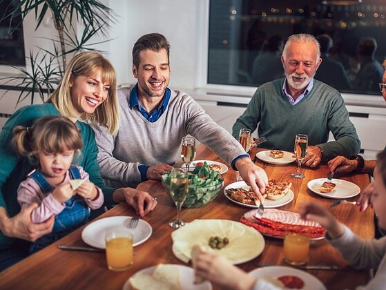 Mehrgenerationen-Familie beim gemeinsamen Essen am Esstisch mit grosser Salatschuessel