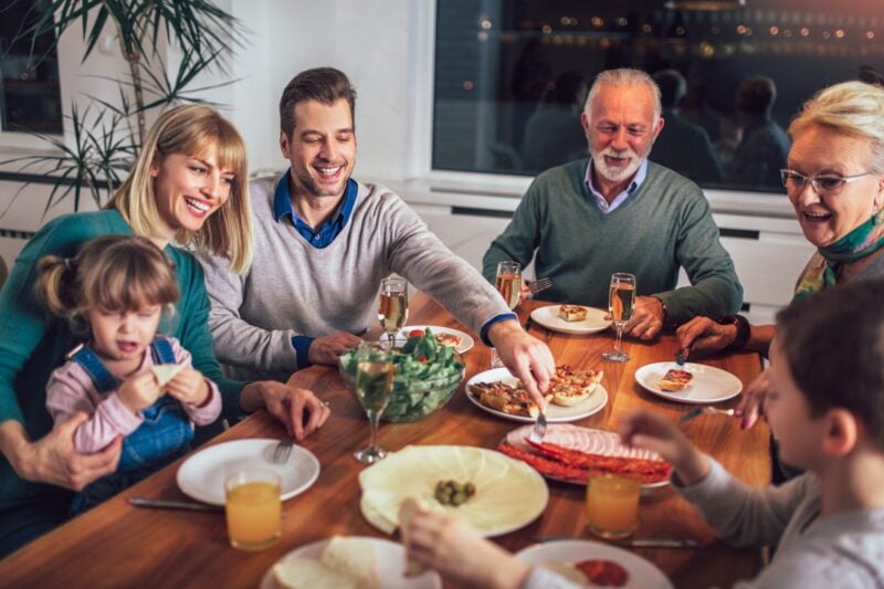 Mehrgenerationen-Familie beim gemeinsamen Essen am Esstisch mit grosser Salatschuessel