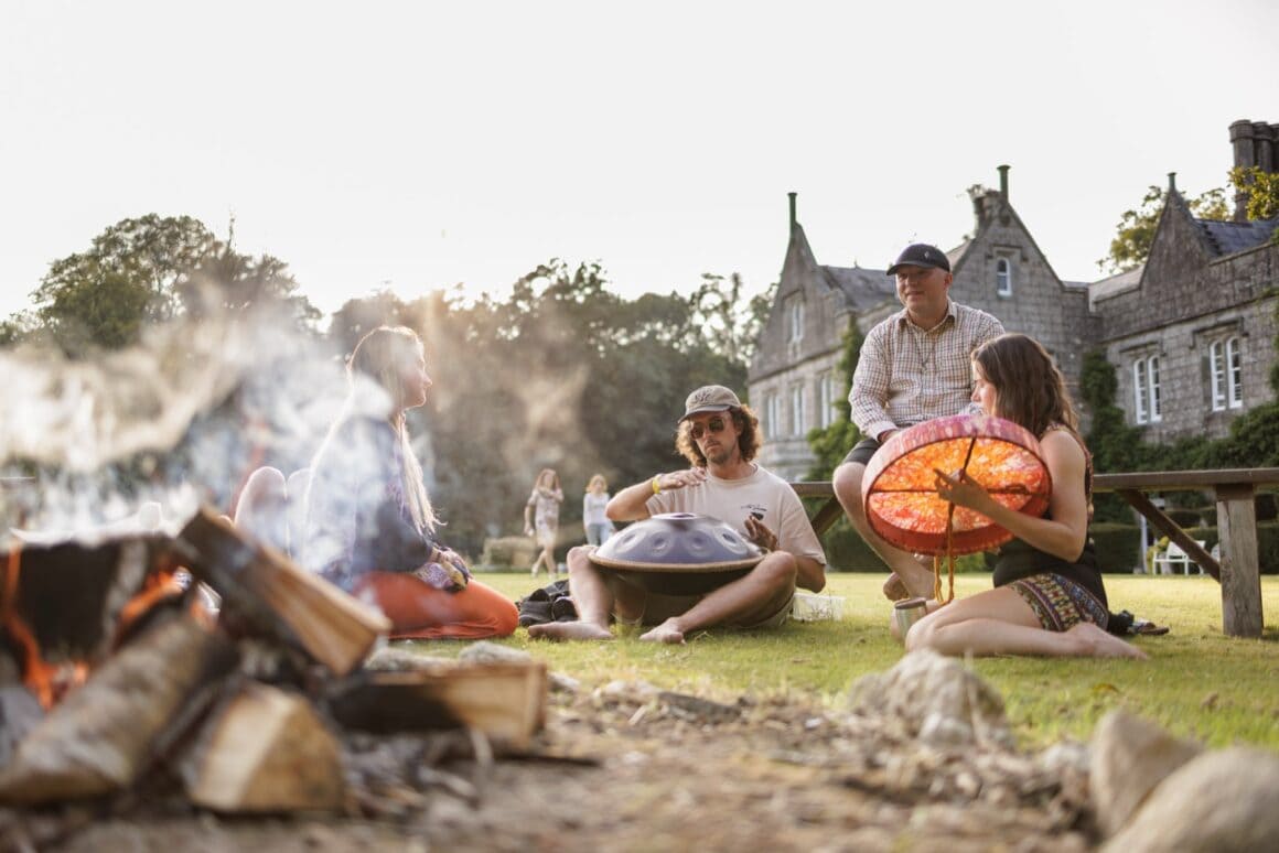 Festivalgäste sitzen bei Sonnenuntergang am Lagerfeuer vor Lisnavagh House beim Féile Vegan in Irland