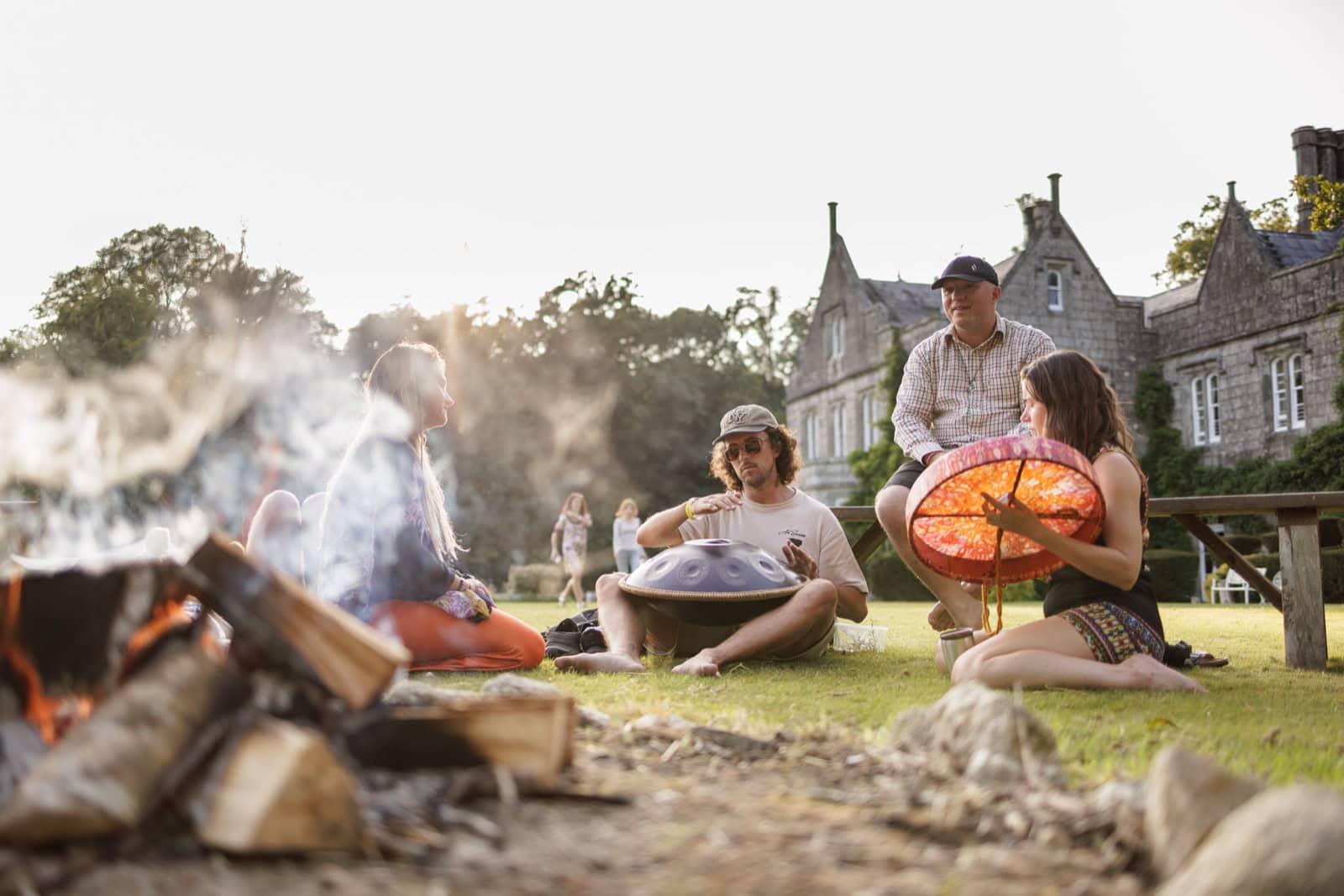 Festivalgäste sitzen bei Sonnenuntergang am Lagerfeuer vor Lisnavagh House beim Féile Vegan in Irland