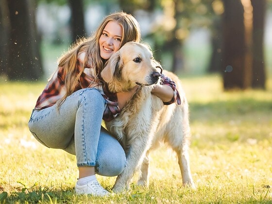 Person umarmt liebevoll ihren Hund auf einer Wiese