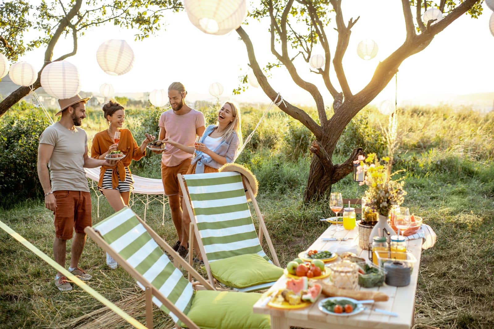Freunde lachen zusammen bei einem sommerlichen Gartenfest mit gedecktem Tisch