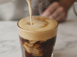 Cremiger Haferdrink wird in eine Tasse Kaffee gegossen und bildet feinen Schaum
