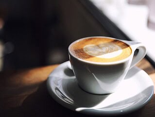 Pflanzlicher Haferdrink wird in eine Tasse Kaffee mit Latte-Art gegossen