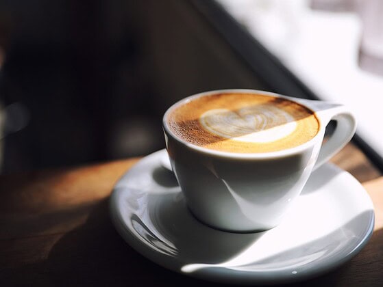 Pflanzlicher Haferdrink wird in eine Tasse Kaffee mit Latte-Art gegossen