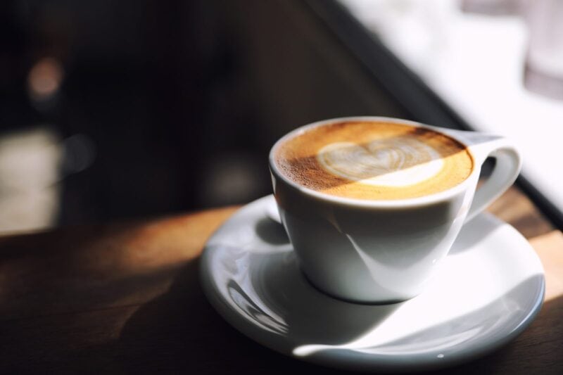 Pflanzlicher Haferdrink wird in eine Tasse Kaffee mit Latte-Art gegossen