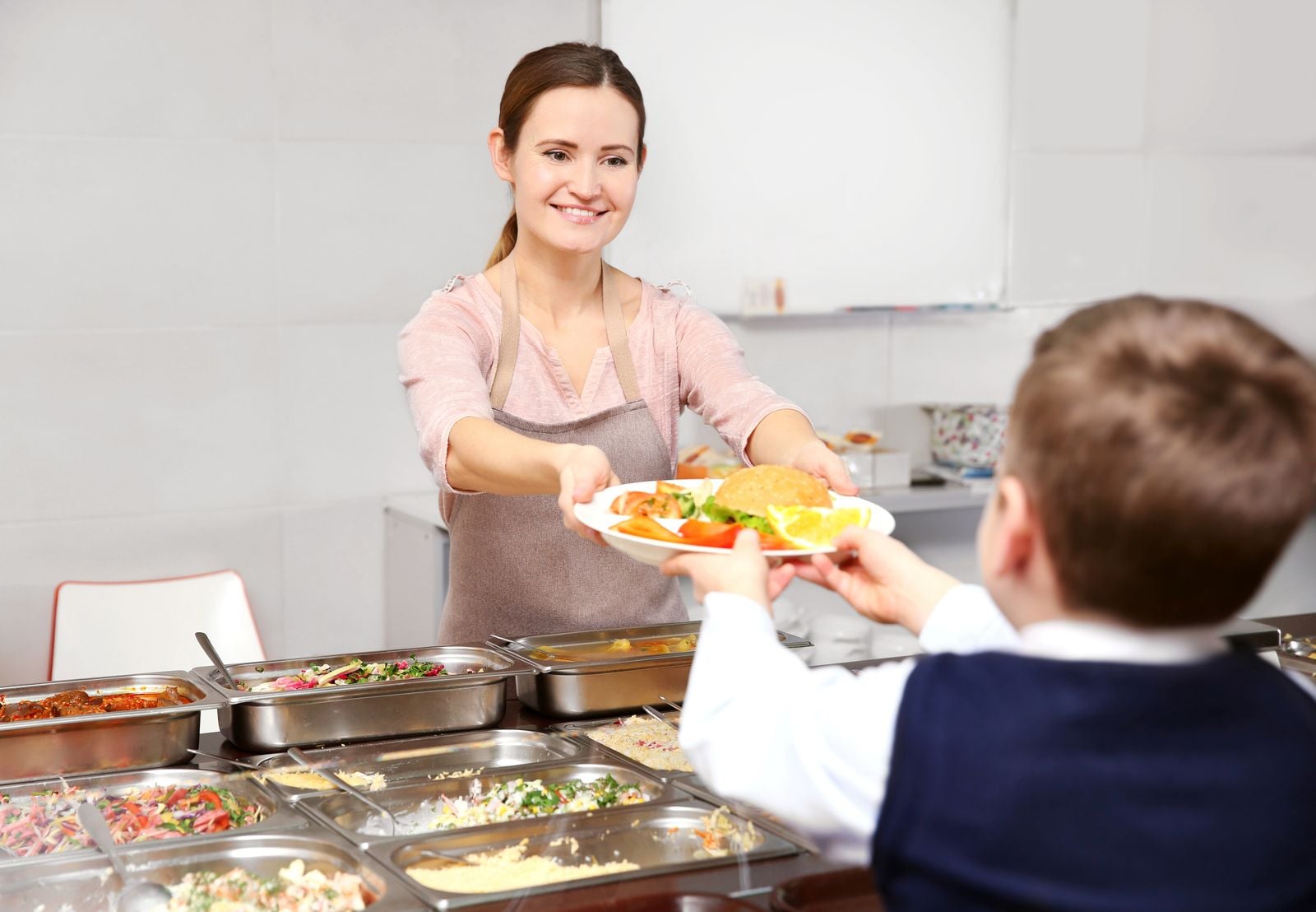 Mitarbeiterin gibt einem Schüler an der Essensausgabe ein Tablett mit Essen