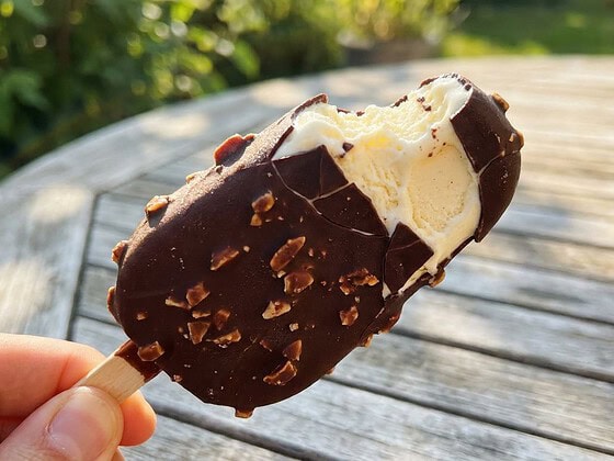 Angebissenes veganes Eis am Stiel mit dunkler Schokoladenhülle und Mandelstückchen