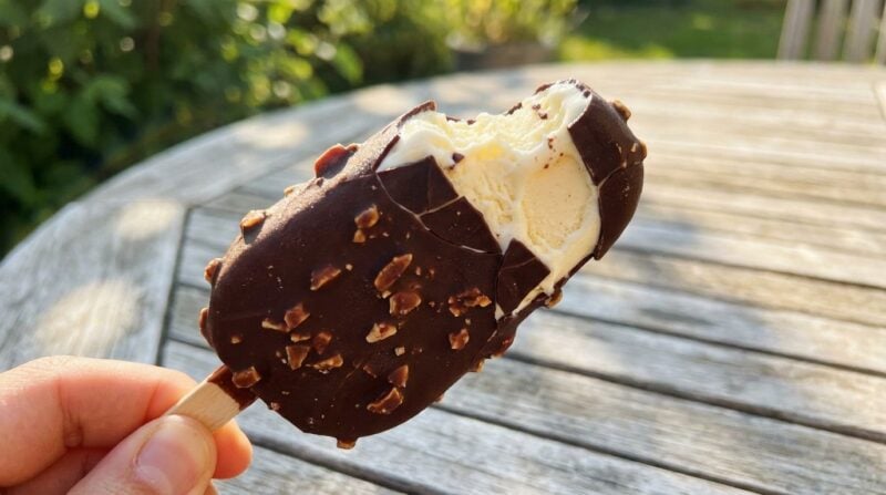 Angebissenes veganes Eis am Stiel mit dunkler Schokoladenhülle und Mandelstückchen