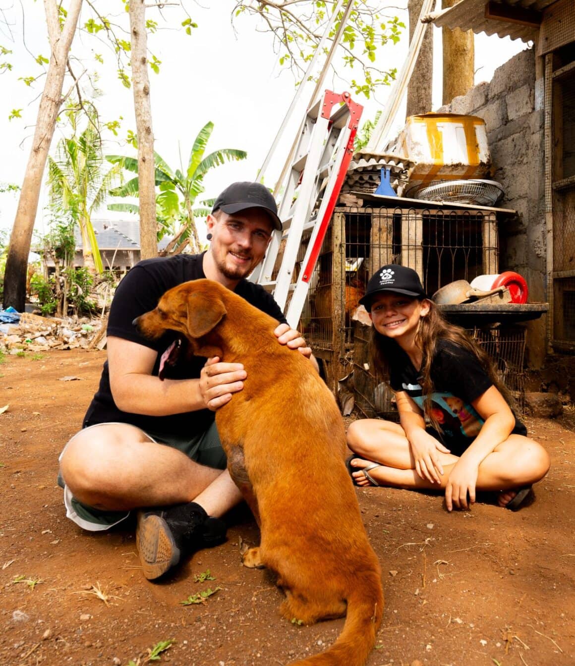 Yannick von This Is Vegan sitzt mit Mia Healing und einem geretteten braunen Hund auf dem Boden ihres Tierheims auf Bali
