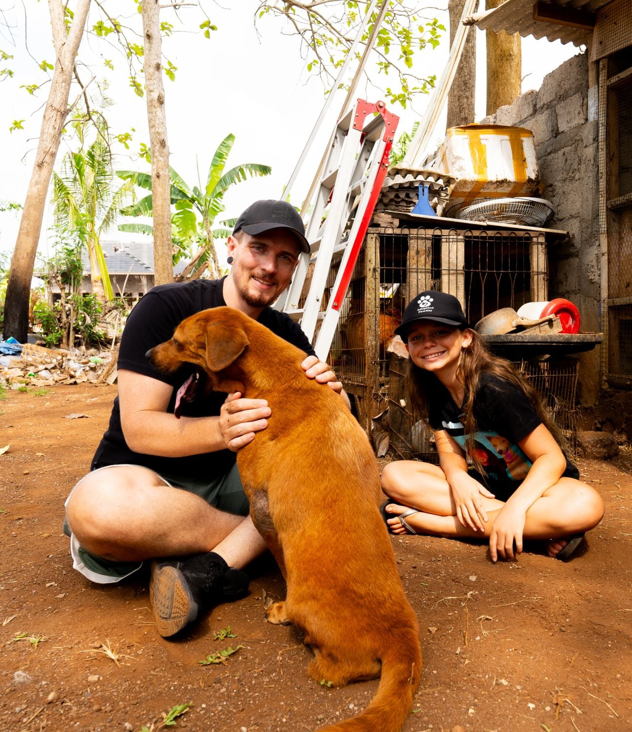 Yannick von This Is Vegan sitzt mit Mia Healing und einem geretteten braunen Hund auf dem Boden ihres Tierheims auf Bali