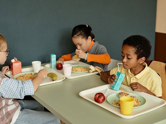 Kinder essen gemeinsam Mittagessen in einer hellen Schulkantine