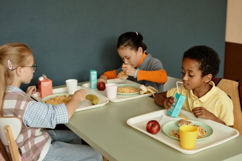 Kinder essen gemeinsam Mittagessen in einer hellen Schulkantine