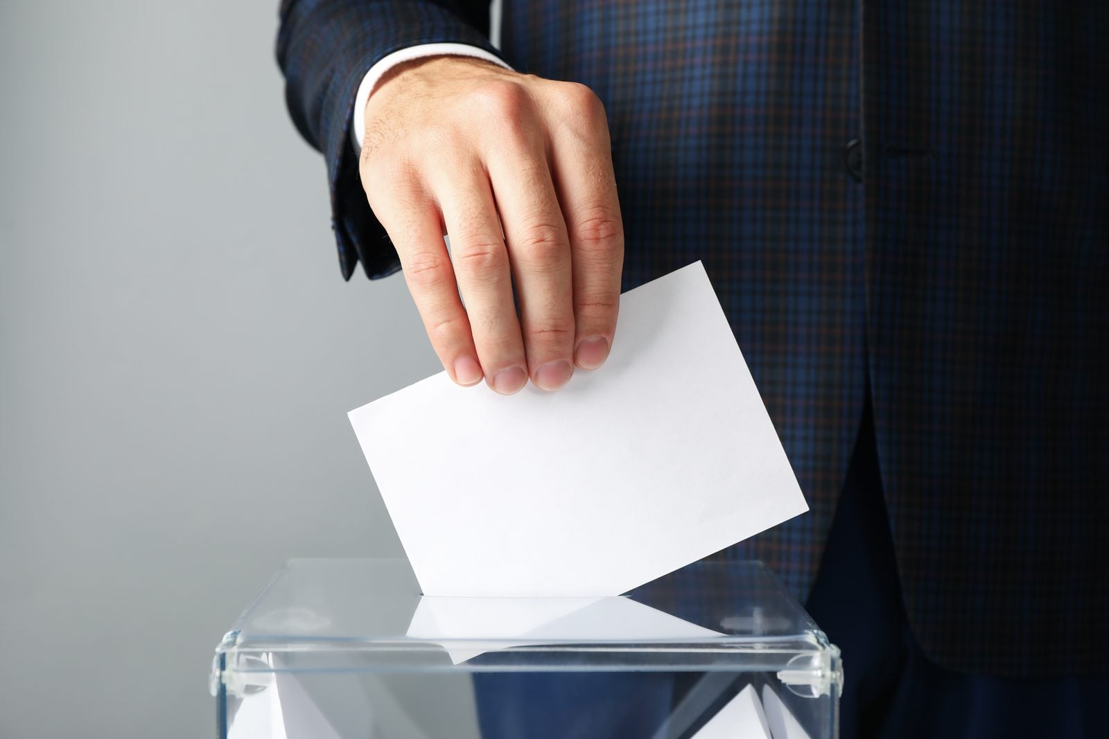 A hand dropping a blank ballot into a transparent voting box