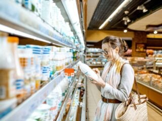 Person steht nachdenklich vor dem Kühlregal im Supermarkt