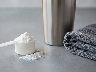 Messlöffel mit Kreatin-Monohydrat-Pulver neben einem Shaker auf einer Steinfläche