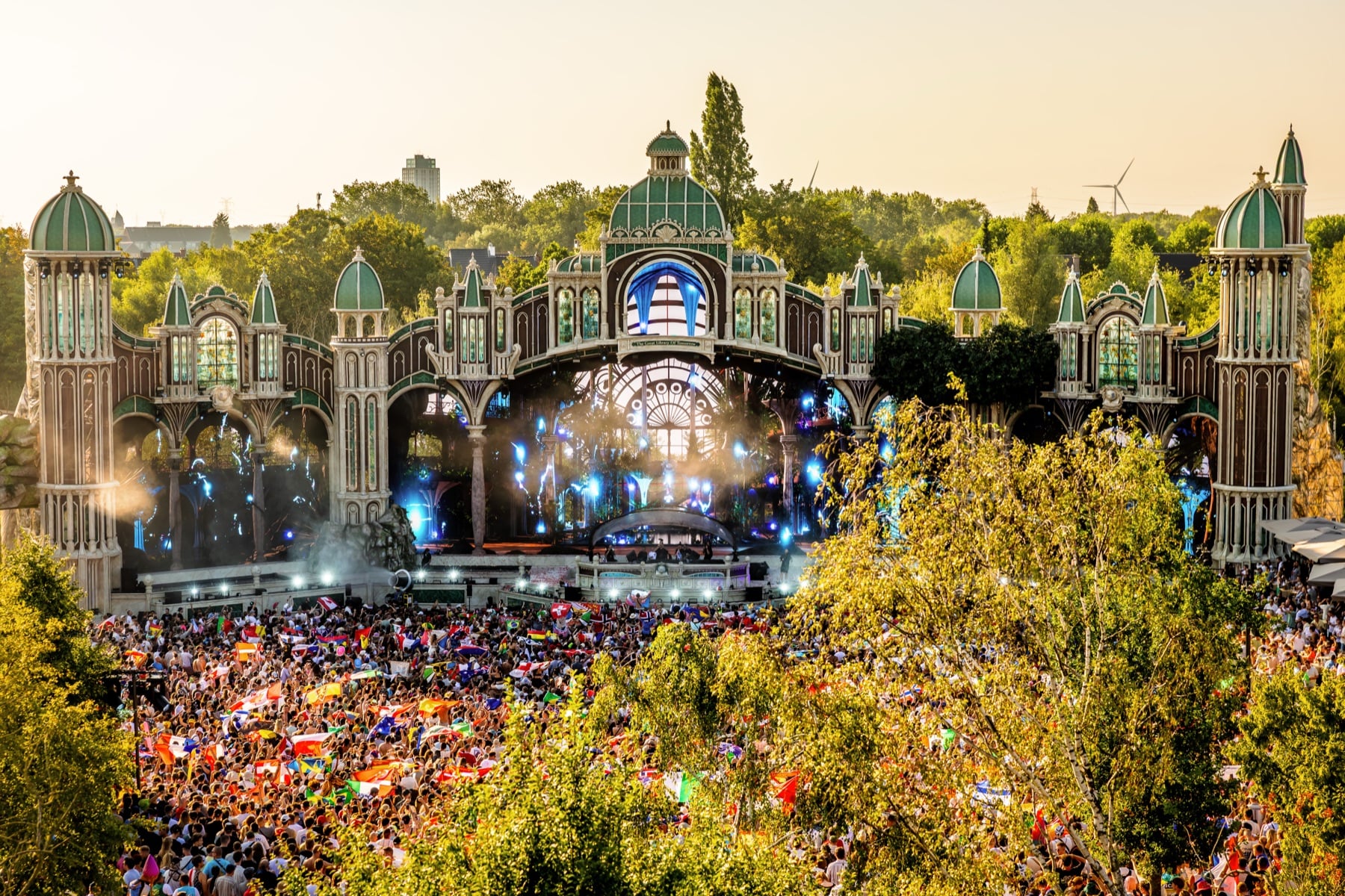 Kunstvoll gestaltete Tomorrowland-Bühne mit grünen Kuppeltürmen zwischen Bäumen im Abendlicht
