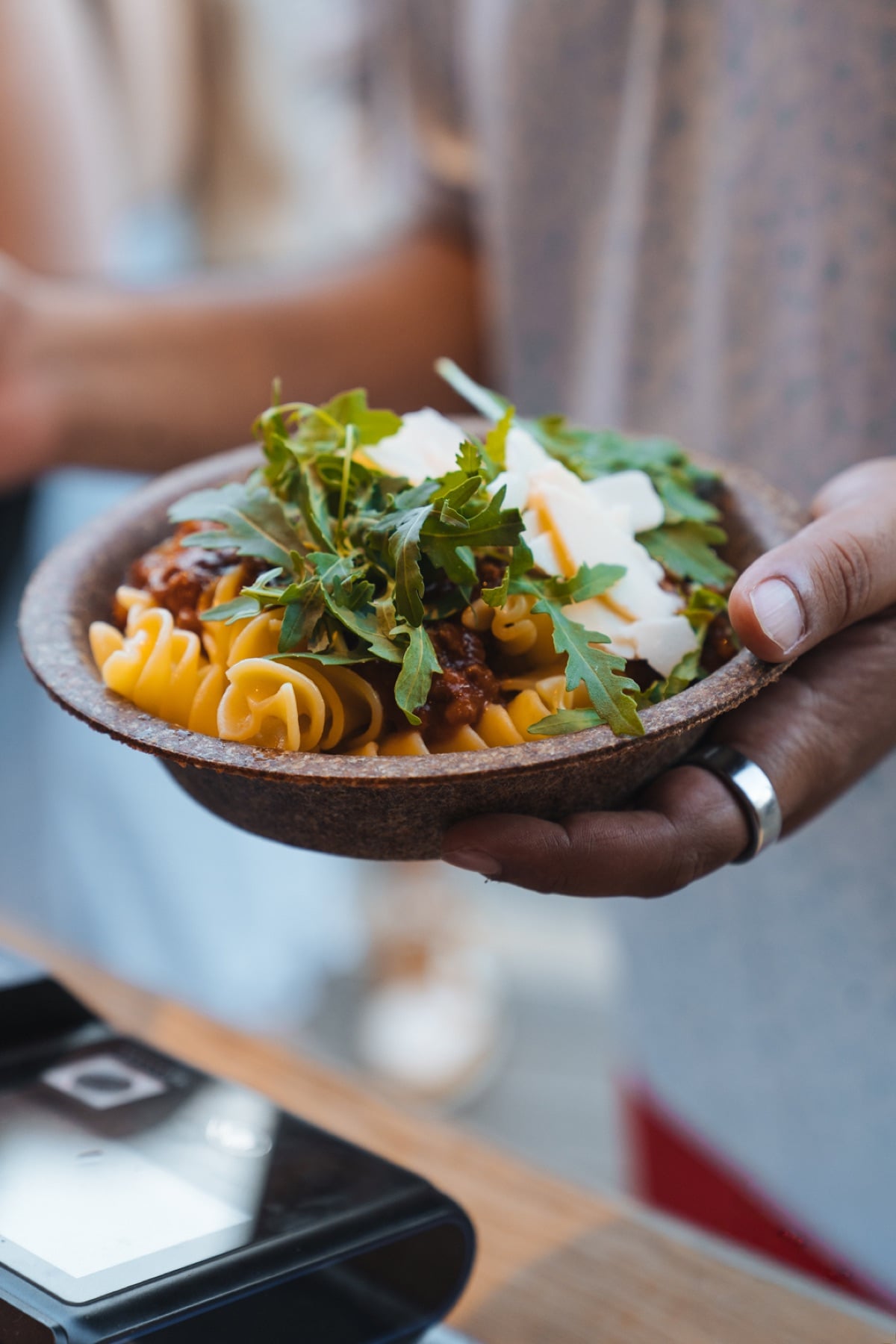 Hand hält eine Pasta-Bowl mit Rucola in einer essbaren Schale an einem Tomorrowland-Foodstand