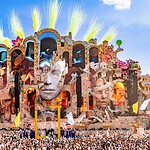 Tomorrowland wird pflanzlich: 70 Prozent fleischfrei bis 2030, PETA will mehr Die Mainstage von Tomorrowland 2026 mit gelben Pyro-Fontänen vor blauem Himmel und riesiger Menschenmenge